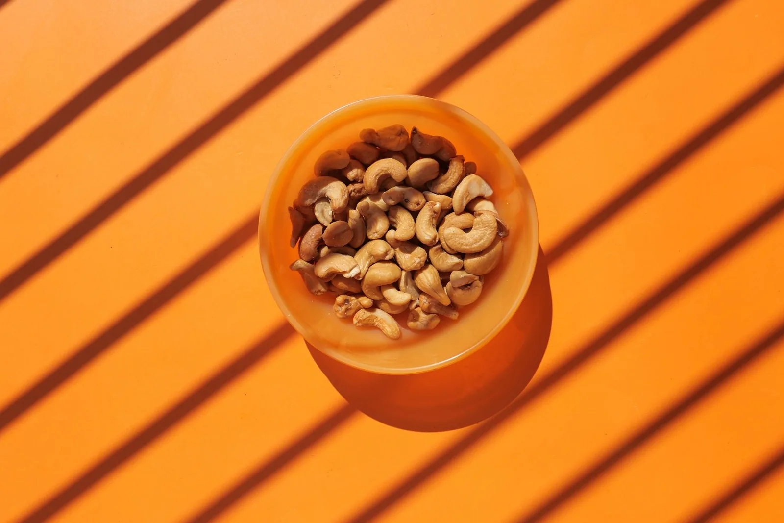 Cashew nuts in an orange bowl on an orange surface