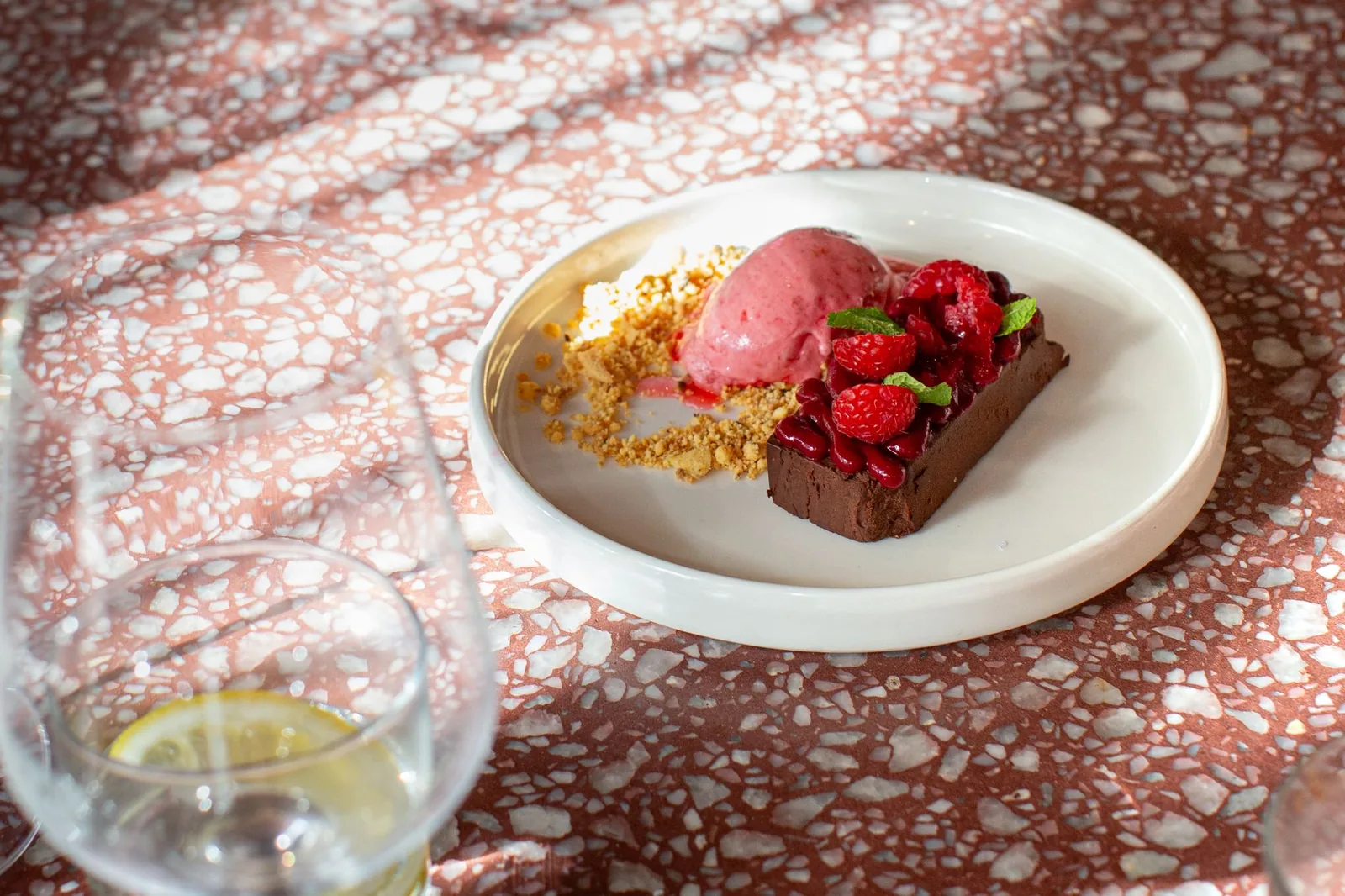 A scoop of pink raspberry sorbet plated beside a chocolate dessert and fresh raspberries.