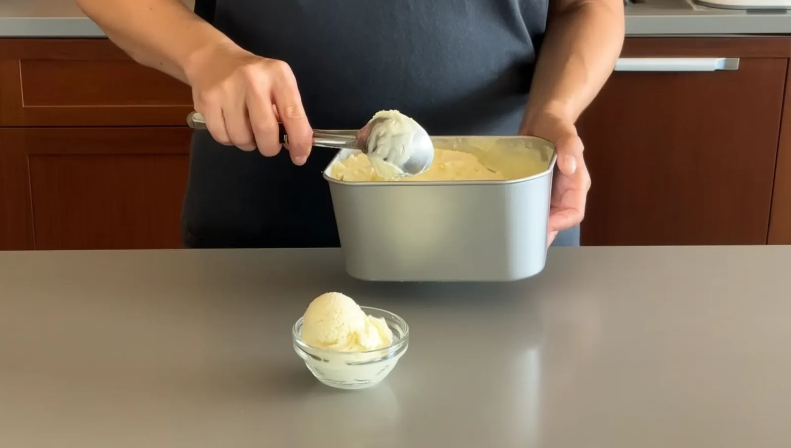 Hands scooping ice cream from a metal tub into a bowl