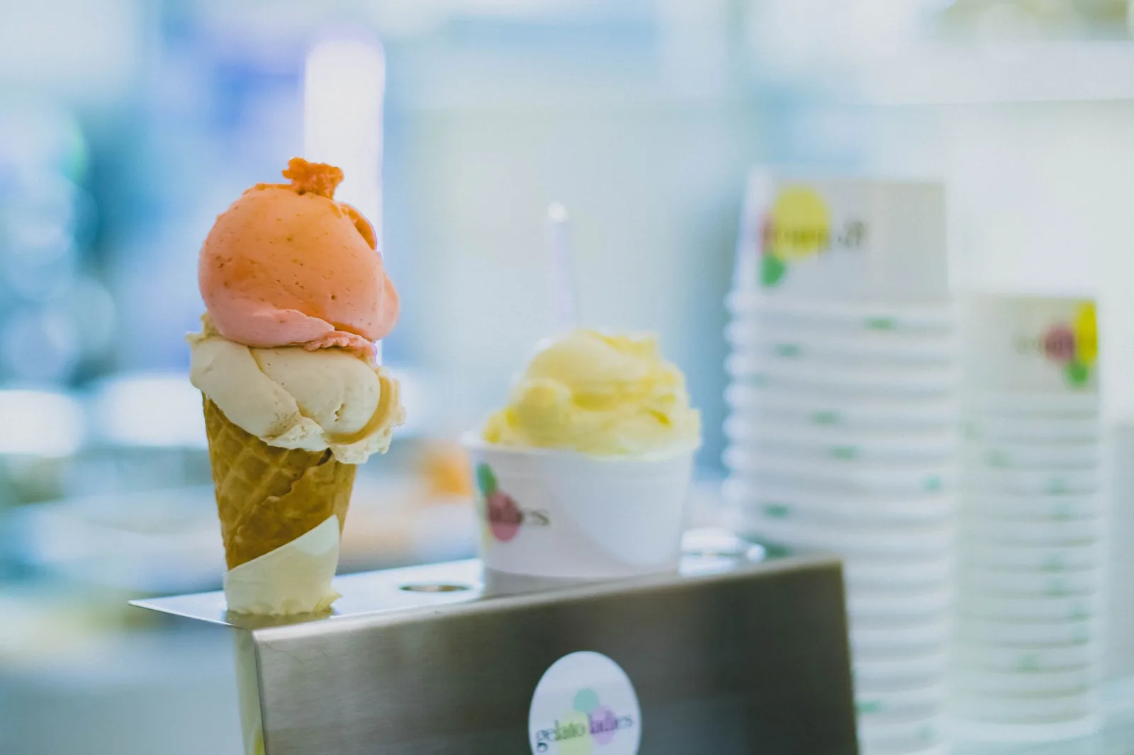 A gelato cone and cup on a gelateria counter