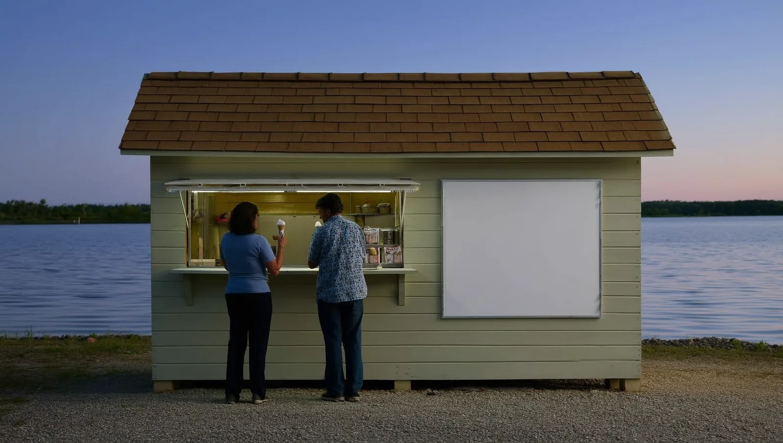 Two people at the open window of a small lakeside ice cream stand