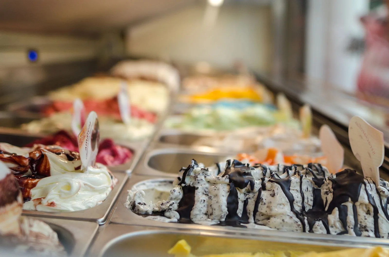 A variety of frozen dessert flavors displayed in a metal freezer case at an ice cream parlor.