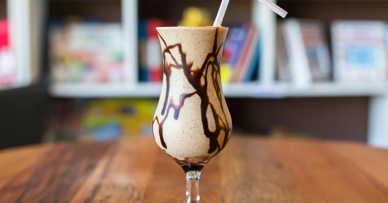 Close-up of a chocolate dairy-free milkshake in a glass with a straw on a wooden table