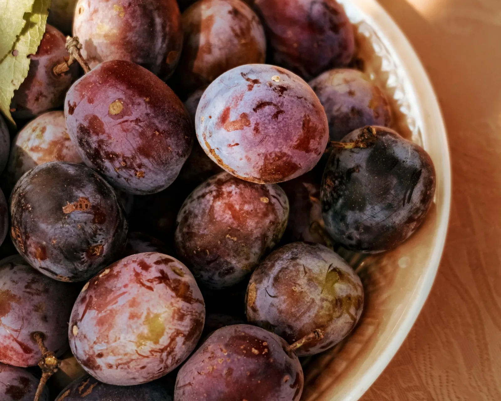 Ripe purple plums piled in a shallow bowl
