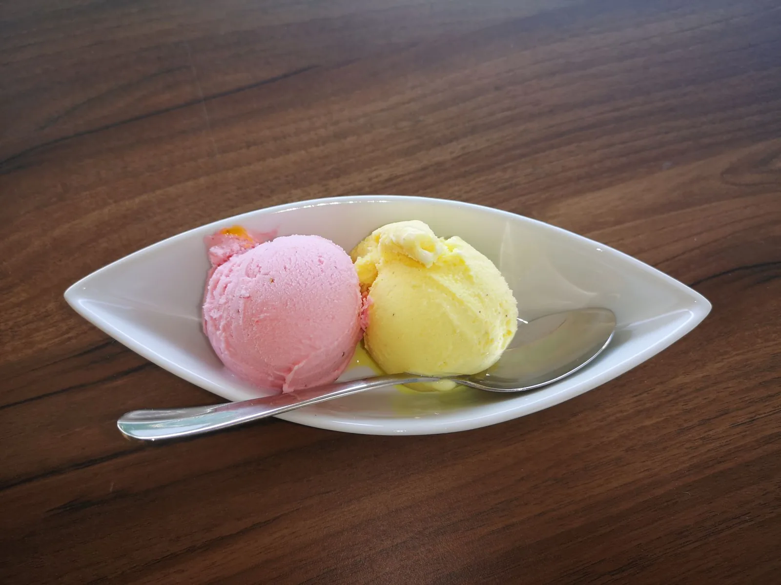 Scoops of ice cream served in a white bowl with a spoon on a wooden table.