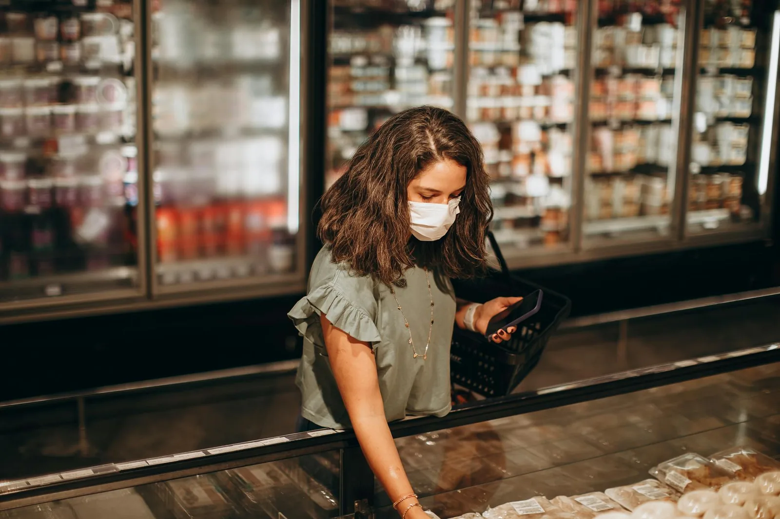 A shopper with a basket choosing items from the freezer aisle of a supermarket.