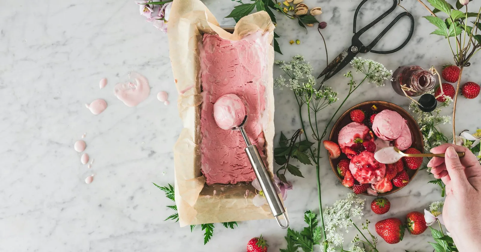 Top-down view of pink ice cream surrounded by fresh berries on a marble surface.