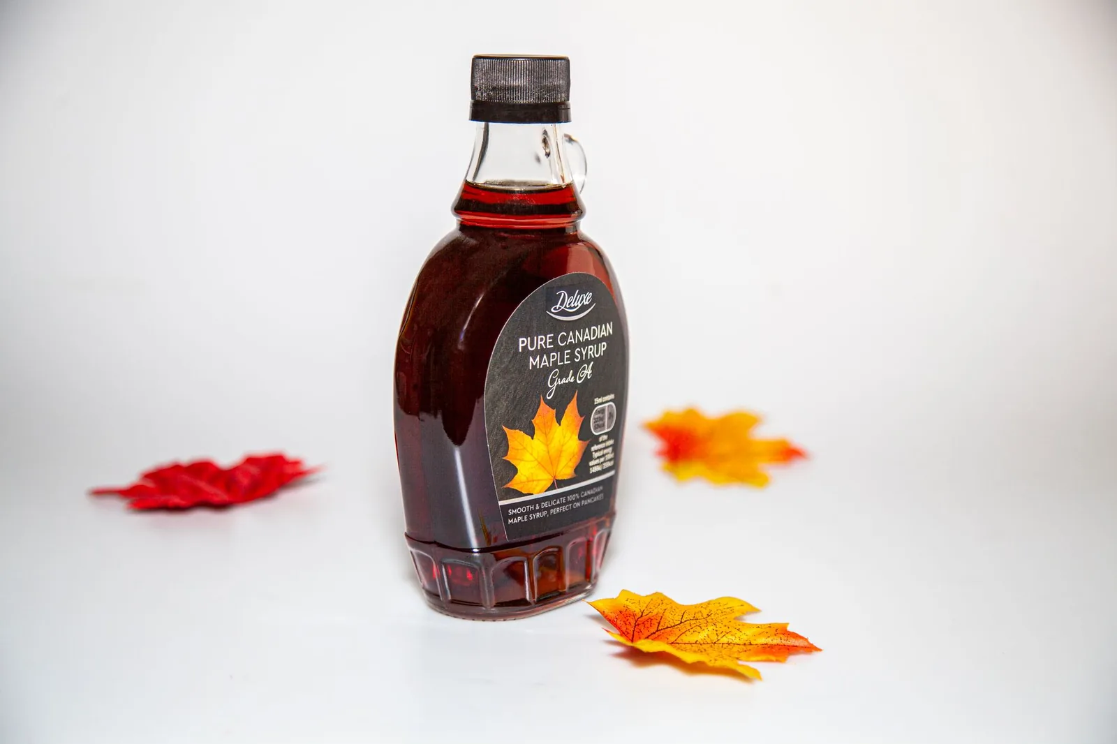A bottle of Canadian maple syrup surrounded by colorful autumn maple leaves.