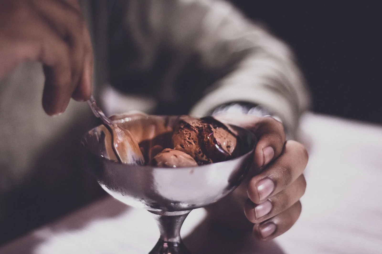 A hand holding a silver bowl of creamy chocolate ice cream.